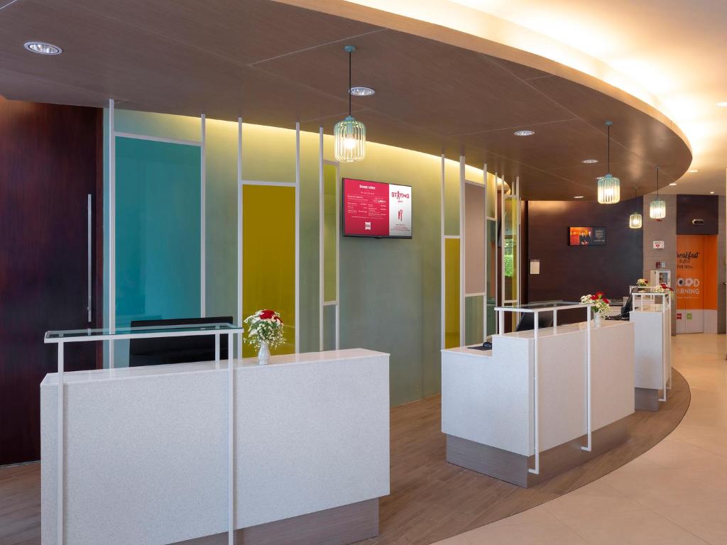 Mūsdienīga viesnīcas reģistratūra ar gaišām krāsām, elegantiem apgaismojuma elementiem un ziedu dekorācijām. Griestu līnijas un struktūras rada patīkamu atmosfēru.