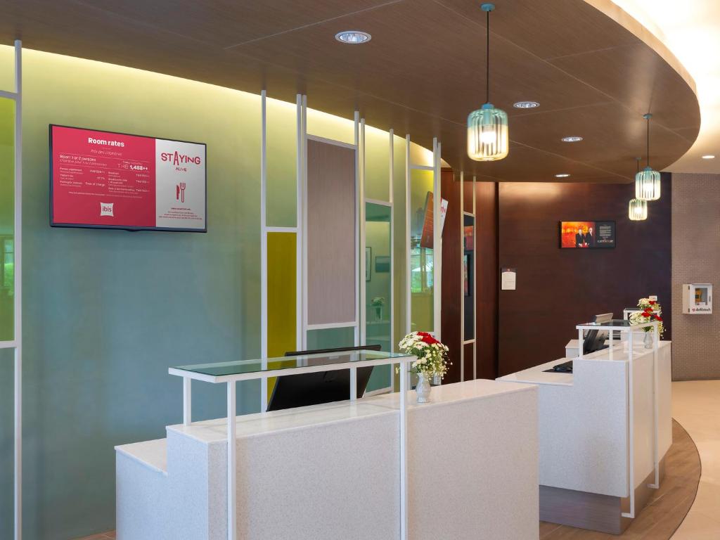 Mūsdienīgs viesnīcas reģistrācijas galds ar interjera elementiem un informatīvu ekrānu, kas parāda viesnīcas numuru cenas. Ziedi pie galda piešķir siltumu un viesmīlību.