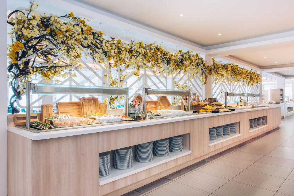 Bufete ar dekoratīvām ziedu kompozīcijām un dažādiem ēdieniem, kas izkārtoti uz koka galda. Gaisīga un mūsdienīga atmosfēra.