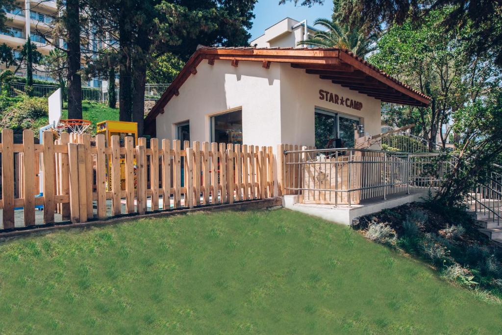 Jauka bērnu nometne ar koka žogu un rotaļu zonu, kas atrodas zaļā apkārtnē. Nometnes ēka ar nosaukumu "STAR CAMP" ir apzaļumota un saulaina.