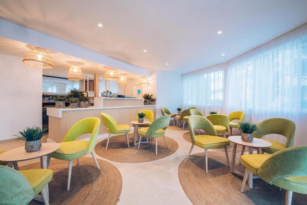 Mūsdienīgs un gaišs kafejnīcas interjers ar zaļām krēslām un apaļiem galdiem, kas veido patīkamu atmosfēru. Interjērā ir radošas lampas un augu dekorācijas.