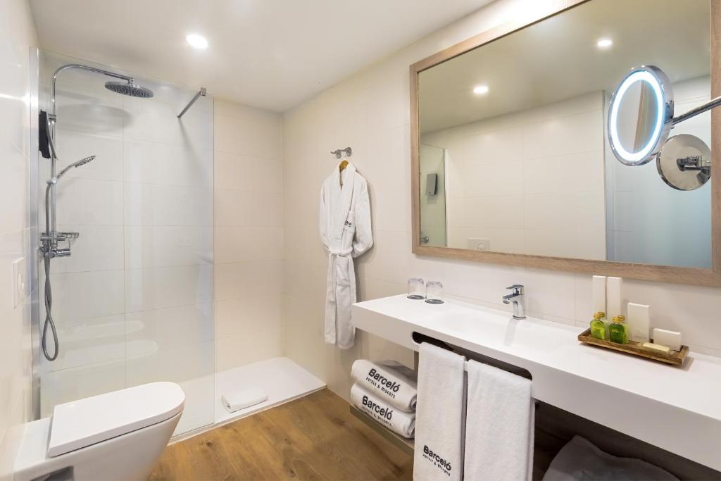 Mūsdienīgs vannas istabas interjers ar stūra dušas kabīni, modernu spoguli un elegantu izkārtojumu. Vannas istabā ir arī dvieļi, higiēnas piederumi un koka grīda.