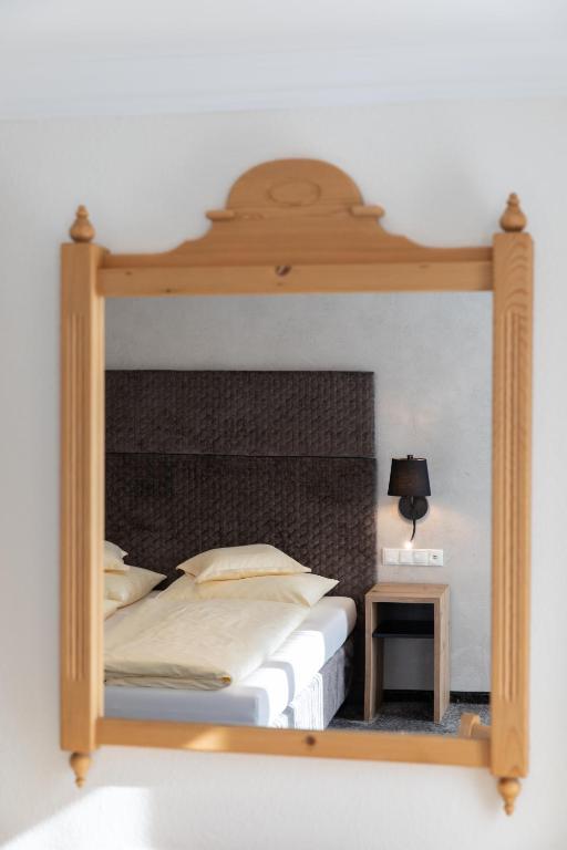 Spoguļa atspulgs viesnīcas numurā ar gultu un naktsgaldiņu, uz kura ir piekārta lampa.