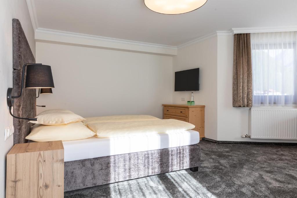 Mūsdienīga guļamistaba ar divguļamo gultu, televizoru un koka mēbelēm, gaišā un ērtā interjerā. Logi ļauj iekļūt dabiskai gaismai, radot patīkamu atmosfēru.