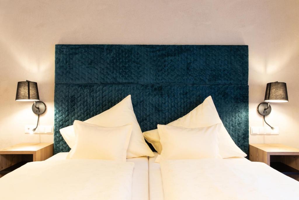 Mūsdienīga guļamistaba ar tumši zaļu gultas galvgalvi un baltiem spilveniem, blakus esošajiem naktsgaldiņiem un lampām. Piemērota relaksācijai un komfortam.