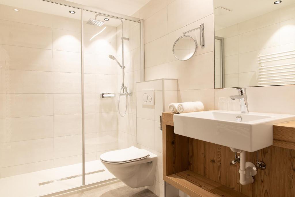 Mūsdienīgs vannas istabas interjers ar dušu, izlietni un tualeti, kas ir veidots no gaišām flīzēm un koka akcentiem.