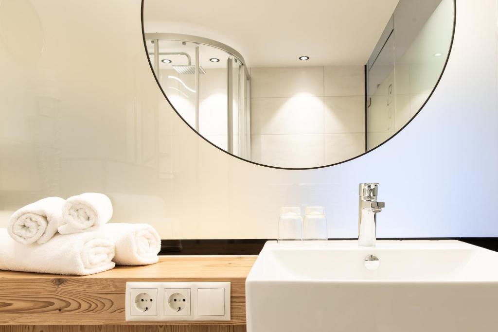 Mūsdienīgs vannas istabas interjers ar baltām dvielēm, sudraba krāsu jaucējkrānu un apaļu spoguļu, kas atspoguļo modernu dizainu.