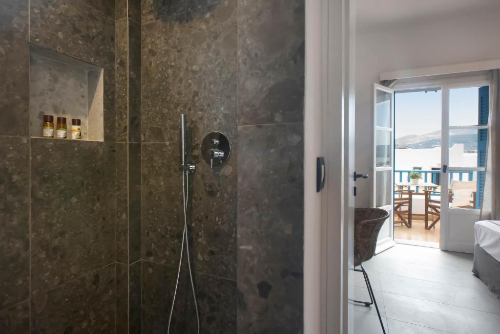 Mūsdienīga duša ar akmens apdari un skatu uz terasi, kurā ir koka mēbeles un gaismas iekārtojums. Duvā atrodas higiēnas piederumi.