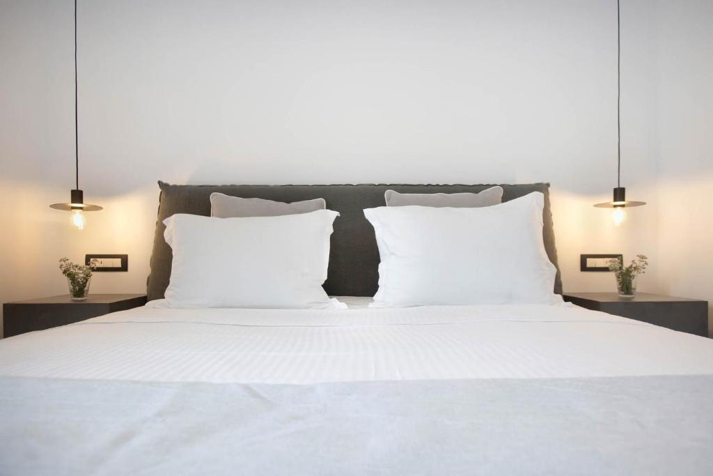 Mūsdienīgs guļamistabas interjers ar ērtu gultu, baltiem spilveniem un stilīgām gaismas ķermeņiem. Blakus gultai atrodas naktsgaldiņš ar nelielu ziedu kompozīciju.