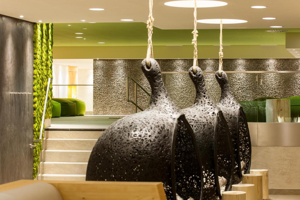 Mūsdienīgs interjers ar trīs melniem mākslas objektiem, kas karājas pie griestiem, un zaļām sienām, kas piešķir telpai dzīvīgumu. Stilīgas kāpnes ved uz nākamo stāvu.