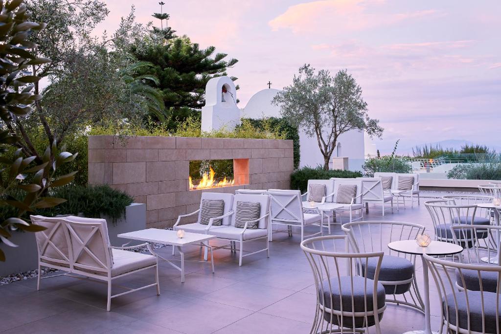 Elegantā terase ar modernām mēbelēm, zāles un ugunskura vietu, kas rada mierīgu atmosfēru. Fons ar vidusjūras stila arhitektūru un dabas elementiem.