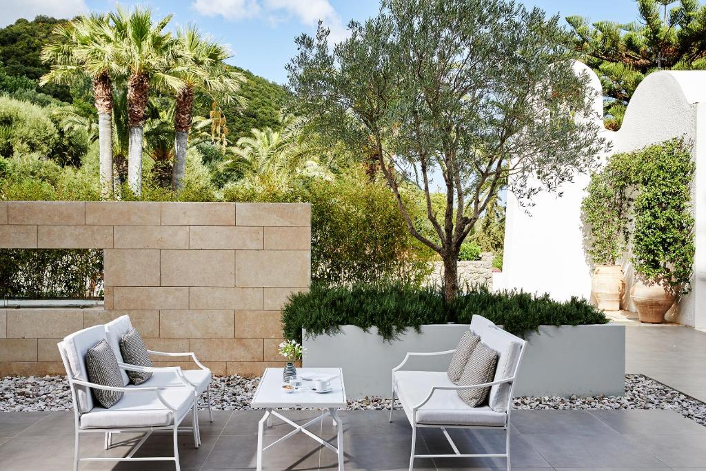 Mūsdienīgs āra terases dizains ar baltām mēbelēm, kas iekārtots starp palmām un zaļumiem. Ideāls relaksācijas stūris, kur baudīt dabu un mieru.