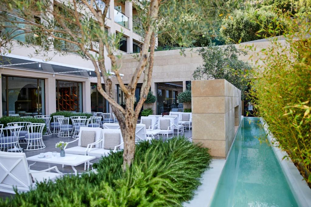 Moderns viesnīcas terases dizains ar elegantiem krēsliem un galdiem, ieskauts zaļumos un ūdens elementiem. Ideāla vieta relaksācijai un atpūtai.