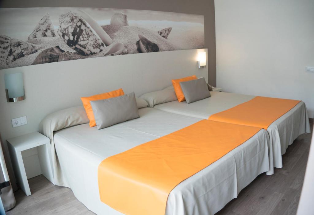 Mūsdienīgs viesnīcas numurs ar divām gultām, kas dekorēts ar oranžām un pelēkām gultas veļām, un izsmalcinātu sienu apdari, kas attēlo pludmales ainavu.