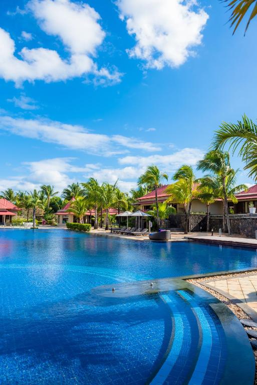 Peldbaseins pie Tamassa Bel Ombre ar palmām un ziliem debesīm.