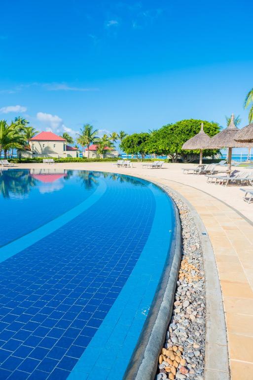 Tamassa Bel Ombre viesnīcas baseins piekrastē, saulains laiks un palmas.