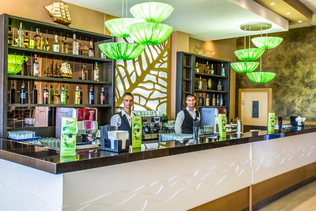 Mūsdienīgs bārs ar zaļām lampām un plašu alkohola izvēli. Bārmeņi apkalpo klientus, radot patīkamu atmosfēru.