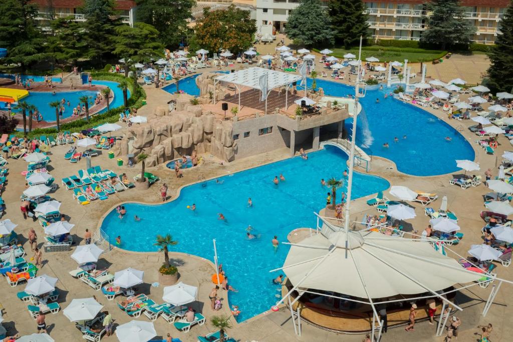 Vasaras atpūtas kūrorts ar vairākiem peldbaseiniem, saulessargiem un cilvēku grupām, kas izbauda ūdens aktivitātes un sauļošanos. Peldbaseini ir apzaļumoti ar palmām un akmeņu veidojumiem.