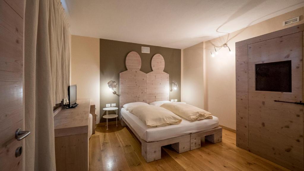 Mūsdienīgs guļamistabas interjers ar koka mēbelēm un divguļamo gultu, kas izceļas ar unikālu galvgali. Telpa ir gaiša un eleganta, ar siltu koka grīdu un mūsdienīgām apgaismojuma iespējām.