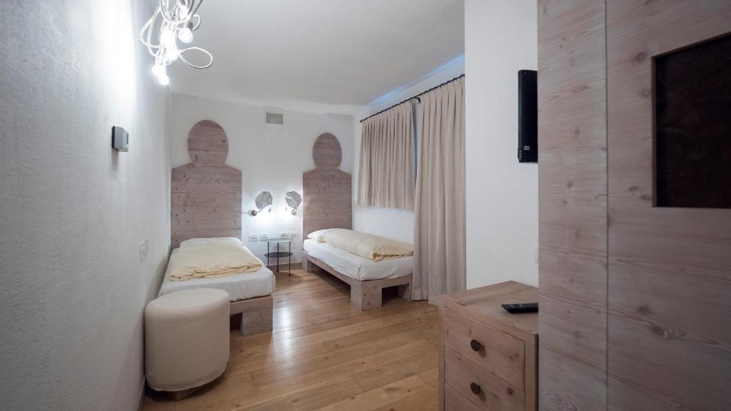 Moderns guļamistabas interjers ar divām gultām, koka mēbelēm un unikāliem sienas elementiem. Telpā ir gaismas ķermeņi un aizkari, radot mājīgu atmosfēru.