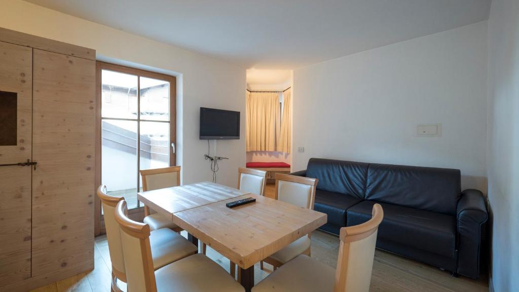 Mūsdienīgs viesistabas un ēdamistabas interjers ar koka galdu, krēslām un dīvānu, kas piedāvā mājīgu atmosfēru. Logi nodrošina dabīgu apgaismojumu un skatu uz ārpusi.