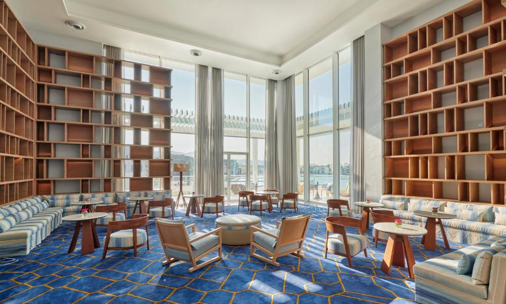 Mūsdienīgs un elegants atpūtas telpas interjers ar gaišām krāsām, ērtiem krēsliem un plašiem logiem, kas nodrošina dabiski apgaismotu atmosfēru. Telpā ir arī lielas grāmatplaukti un stilīgas mēbeles.