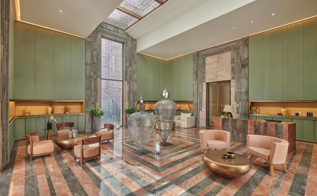 Mūsdienīgs viesnīcas vestibils ar elegantu interjeru, kas ietver zaļas sienas un marmora grīdu, kurā redzami dizaina krēsli un dekoratīvi elementi.