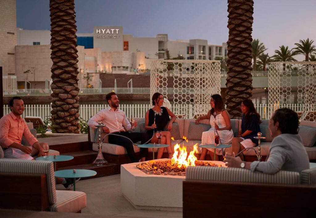 Sociāla sanākšana pie ugunskura modernā āra vidē, kur cilvēki izbauda vakaru pie Hyatt Regency viesnīcas.