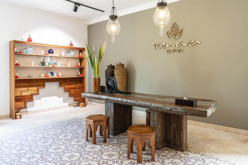 Spa pieņemšanas zona ar elegantu koka galdu, stilīgām lampām un dekoratīviem elementiem, kas rada relaksējošu atmosfēru. Uz sienas redzams "Renova Spa" logo.