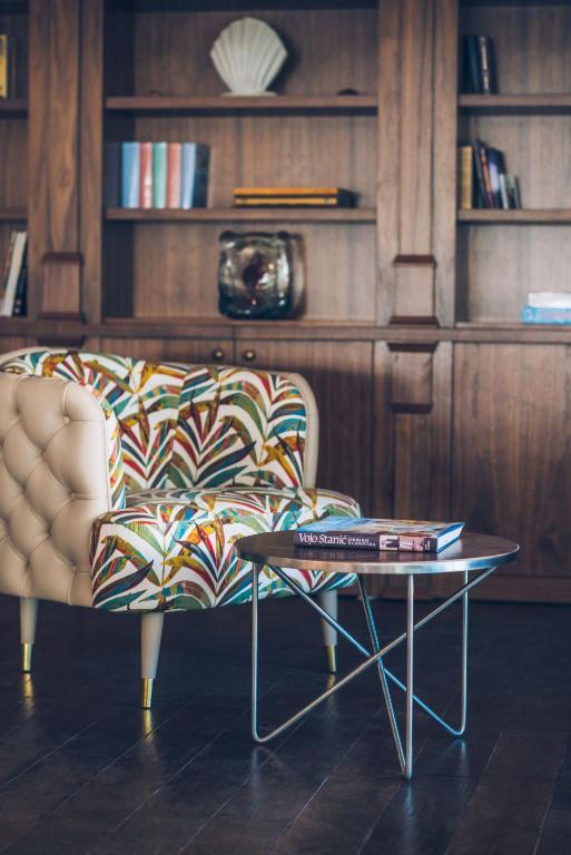 Krāsains, moderns dīvāns ar ziedu rakstu un metāla galdiņš, kas atrodas pie grāmatu plaukta. Interjers piedāvā elegantu un mājīgu atmosfēru.