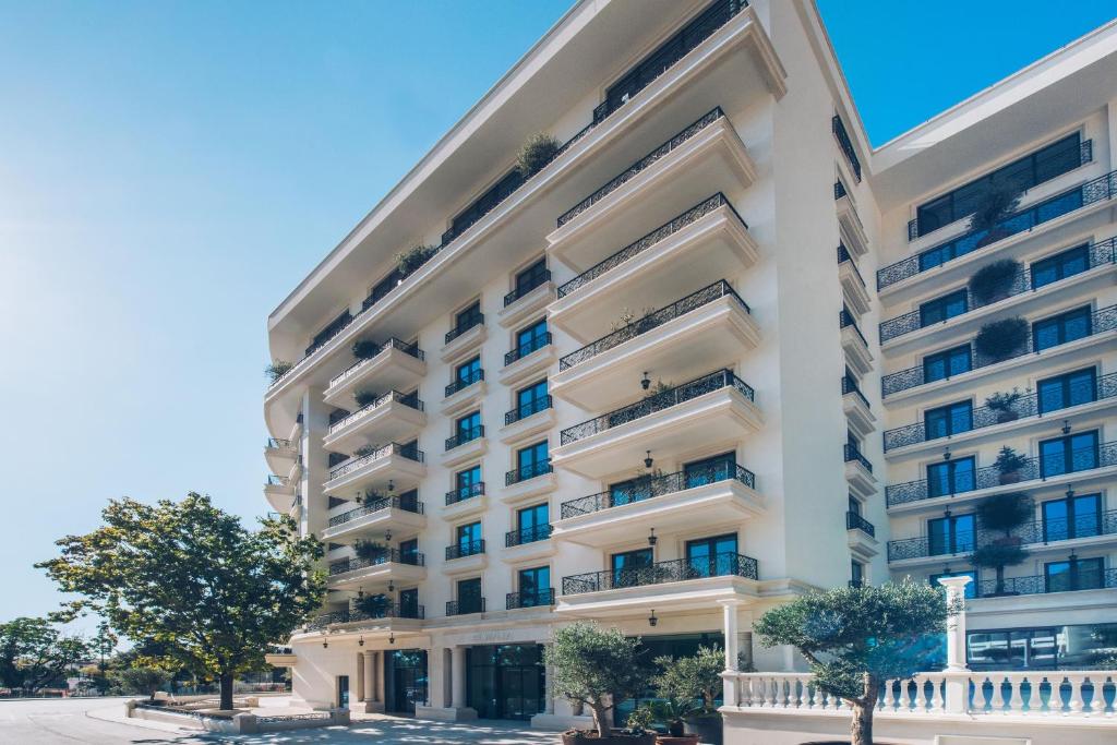 Moderns viesnīcas ēkas dizains ar plašiem balkoniem un ziediem, kas rotā fasādi. Gaismas un ēnu spēle piešķir ēkai elegantu izskatu.