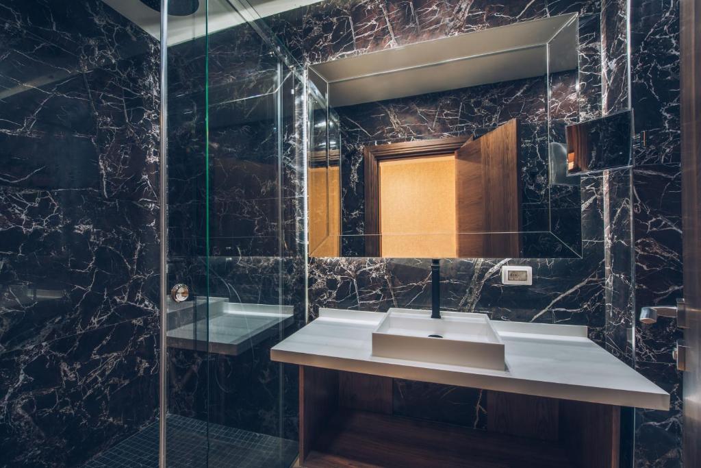 Mūsdienīgs vannas istabas interjers ar melnu marmora apdari un stikla dušu. Uz galda atrodas elegants izlietnes dizains.