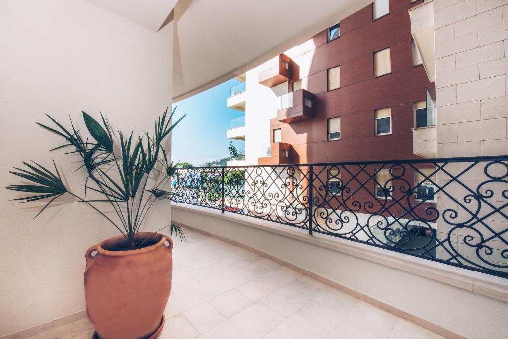 Balkons ar zaļu augu un dekoratīvu metāla margu, kas vērsts uz blakus esošiem moderniem ēkām. Svaiga gaisa un saules gaismas piesātināta telpa.