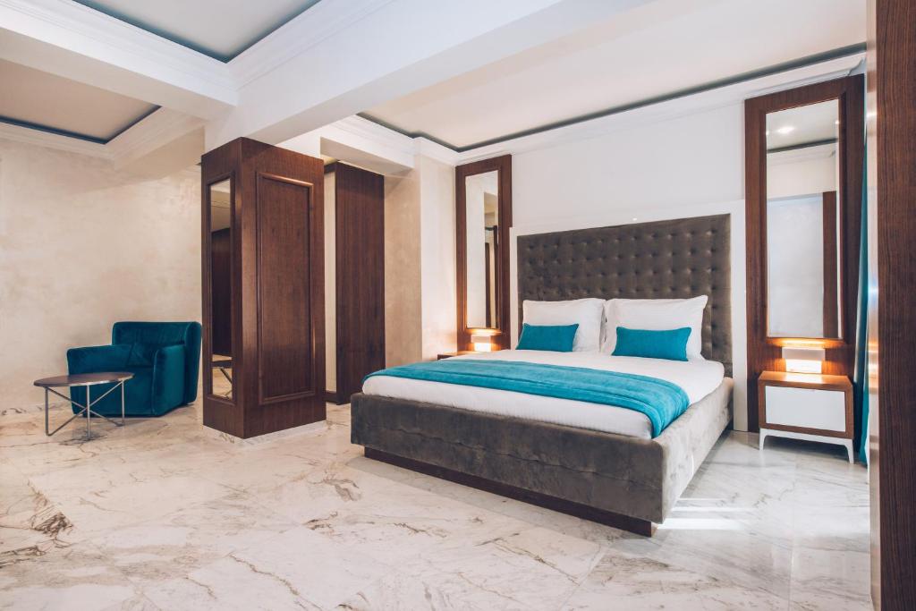 Mūsdienīga guļamistaba ar elegantu dizainu, kurā ir liela gulta ar mīkstu galvgalu un spilveniem, kā arī komfortabla zila krēsla zona un spoguļi. Grīda ir izklāta ar elegantām marmora flīzēm.