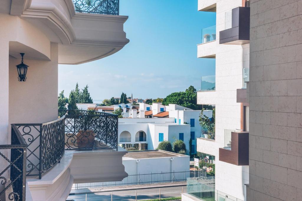 Balcony view of modern architecture with white buildings and blue accents, framed by wrought iron railings and greenery under a clear sky.