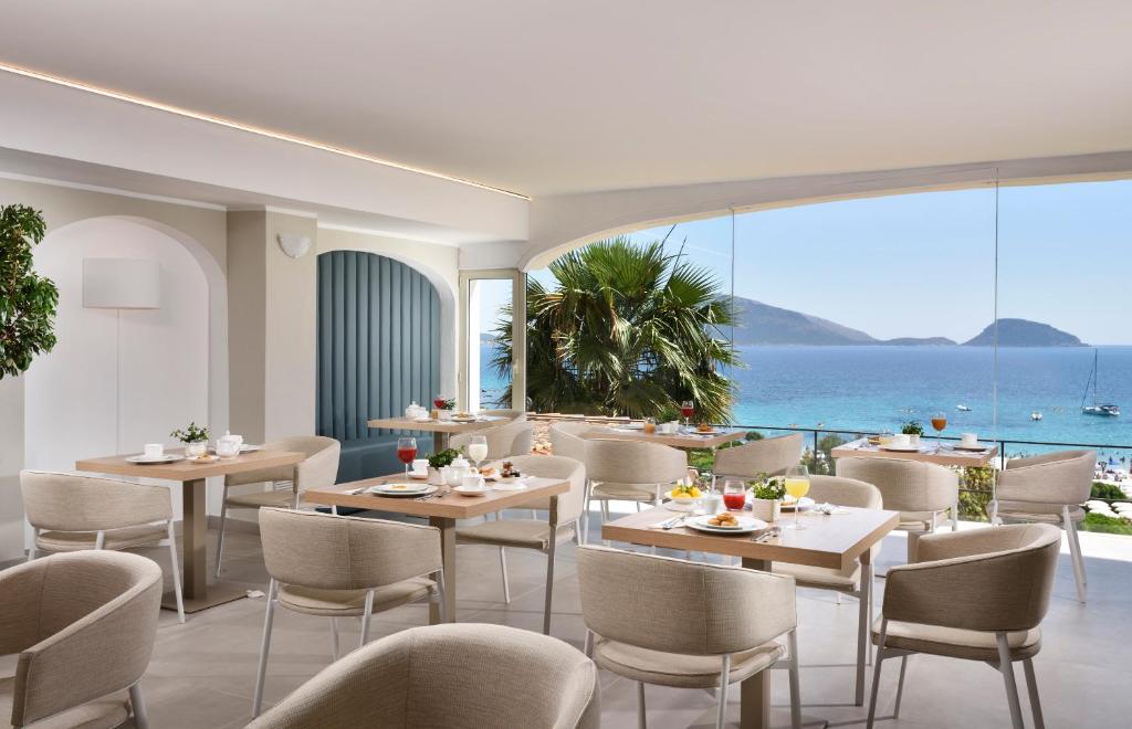 Mūsdienīgs restorāns ar skatu uz jūru, kurā ir eleganti galdi un krēsli, piedāvā gardas brokastis. Gaisīgs interjers ar plašām logu daļām un zālēm, kas izrotātas ar zaļumiem.