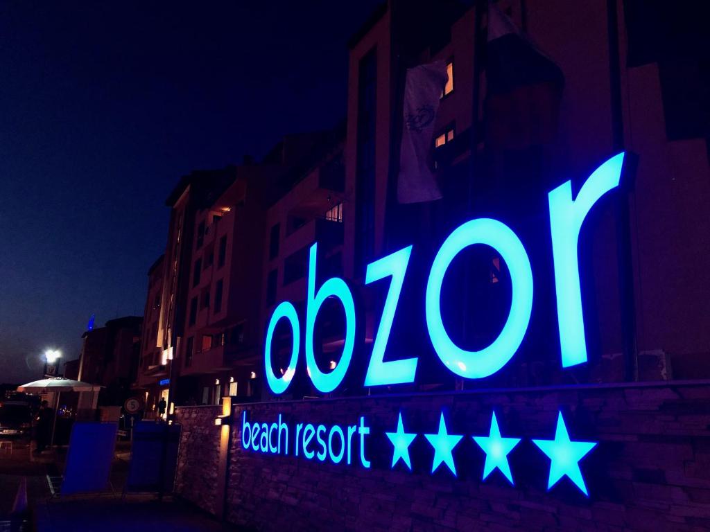 Obzor pludmales kūrorts ar spožu, zilu apgaismojumu, kas izgaismo nakts ainavu. Kūrorta nosaukums ir redzams lielos burtos.