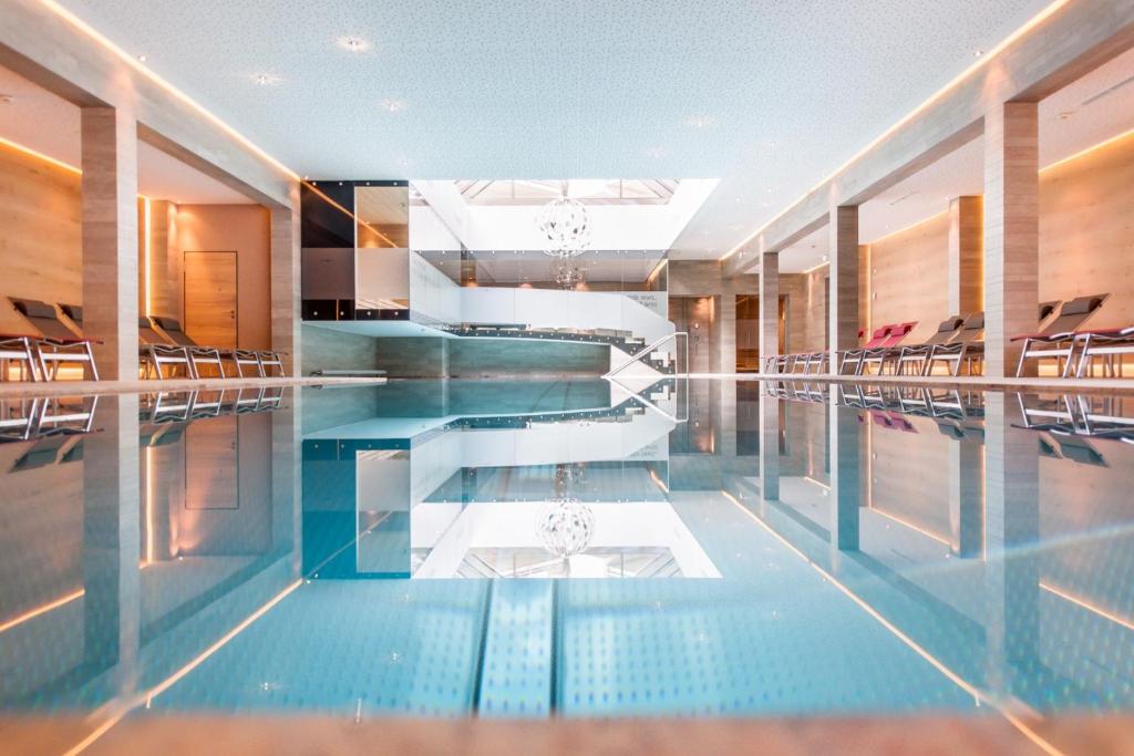Mūsdienīgs peldbaseins ar elegantu interjeru un atspulgu ūdenī, kas rada relaksējošu atmosfēru. Apgaismojums un arhitektūras elementi piešķir telpai stilīgu izskatu.