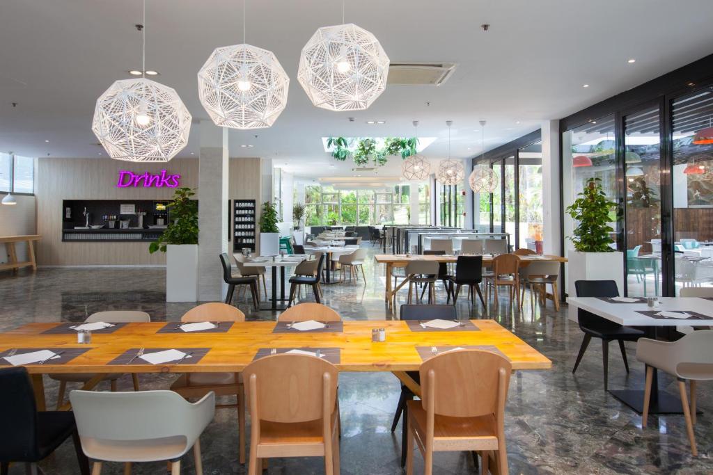 Mūsdienīgs restorāns ar elegantu interjeru, kurā ir koka galdi un stilīgas lampas. Gaismas un zaļi augi rada patīkamu atmosfēru.