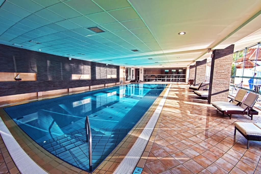 Iekštelpu peldbaseins ar modernu dizainu un saulainu apgaismojumu, ap kuru izvietoti atpūtas krēsli.