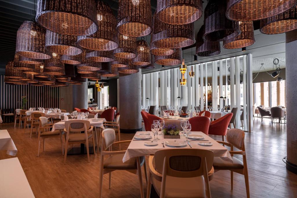 Mūsdienīgs restorāns ar elegantu interjeru, kurā redzami pušķi un stilīgas lampas. Gaisīga atmosfēra un rūpīgi sakārtotas galdi, kas rada patīkamu ēdināšanas pieredzi.