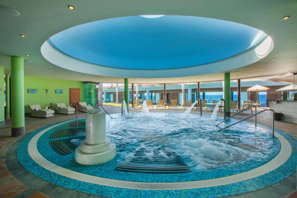 Mūsdienīgs spa ar apaļu baseinu un ūdens plūsmām, ko izgaismo dabiska gaisma no jumta. Viegla un relaksējoša atmosfēra ar komfortablām atpūtas vietām.