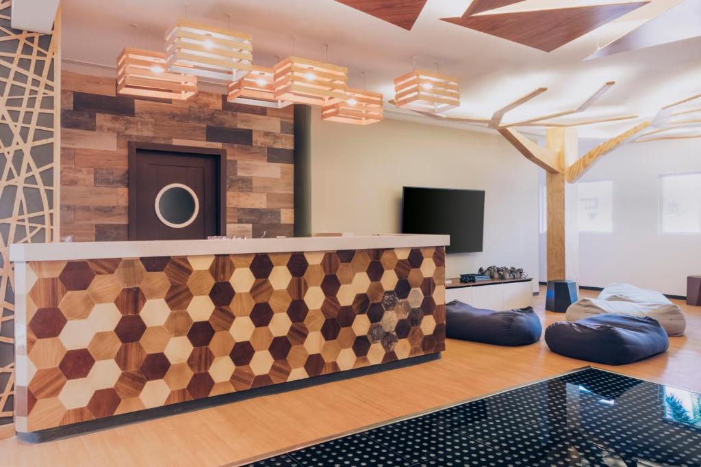 Mūsdienīgs reģistratūras dizains ar ģeometriskām koka detaļām un stilīgām gaismas ķermeņiem. Telpa ir aprīkota ar komfortablām sēdvietām un lielu televizoru.