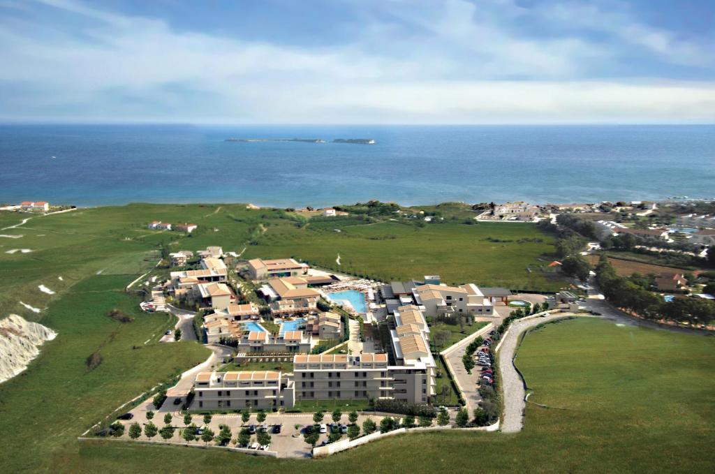 Klusais kūrorts pie jūras ar zaļām pļavām un baseinu. Skats no augšas, kas parāda viesnīcu kompleksu un apkārtējo ainavu.