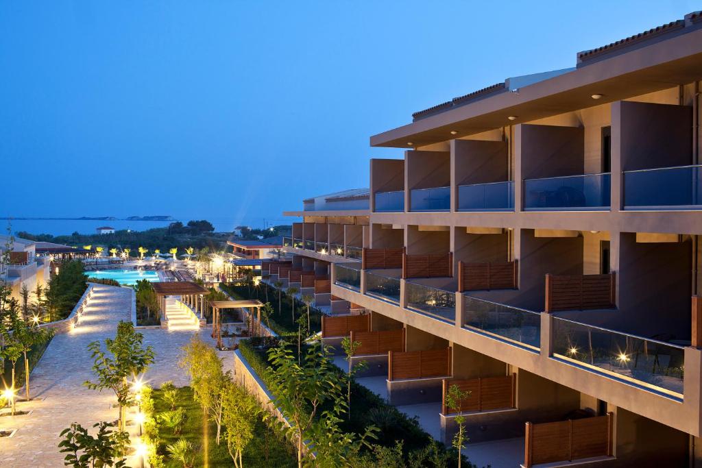 Mūsdienīgs viesnīcas komplekss ar apgaismotu teritoriju un baseinu, kas redzams vakara gaismā. Apkārtne ir rūpīgi kopta ar augiem un ainavu elementiem.