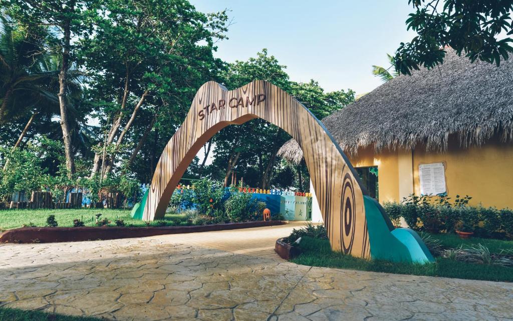 Ieejas arka "Star Camp" ar zaļo vidi un krāsainu arhitektūru, kas attēlo viesmīlīgu un jautru atmosfēru.