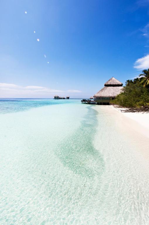Tīras, kristāldzidras ūdens plūsmu un balta pludmale ainava, kas veido tropisku paradīzi ar mājīgu mājiņu uz mola.
