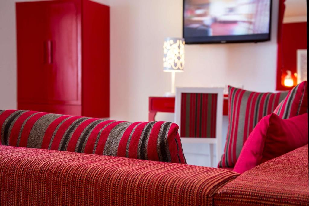 Sarkanas un melni svītrains dīvāns ar spilveniem, moderns interjers ar televizoru un lampu. Aiz dīvāna redzama sarkana skapja un balta krēsla kombinācija.