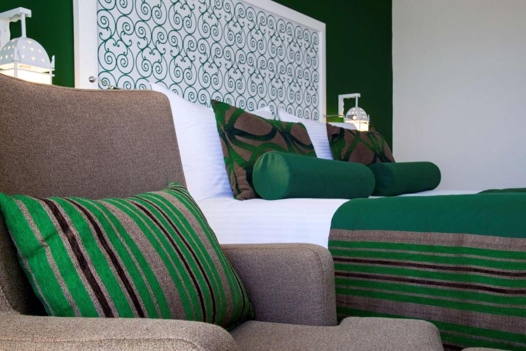 Mūsdienīga viesnīcas istaba ar zaļām un brūnām detaļām, iekārtota ar komfortablu krēslu un spilveniem. Istaba izceļas ar dekoratīvu fona sienu un patīkamu atmosfēru.