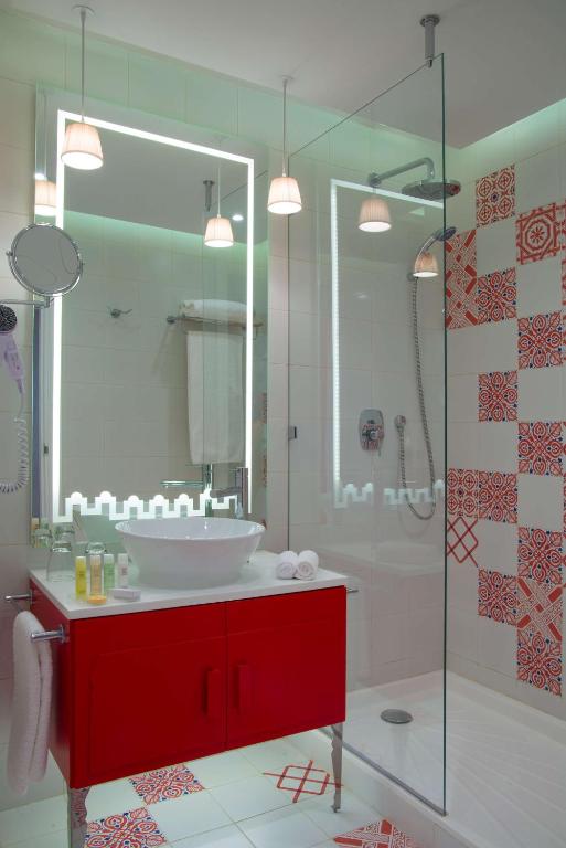 Mūsdienīgs vannas istabas iekārtojums ar sarkano skapīti un radošu flīžu dizainu. Iekļautas modernās apgaismojuma un vannas aksesuāru detaļas.
